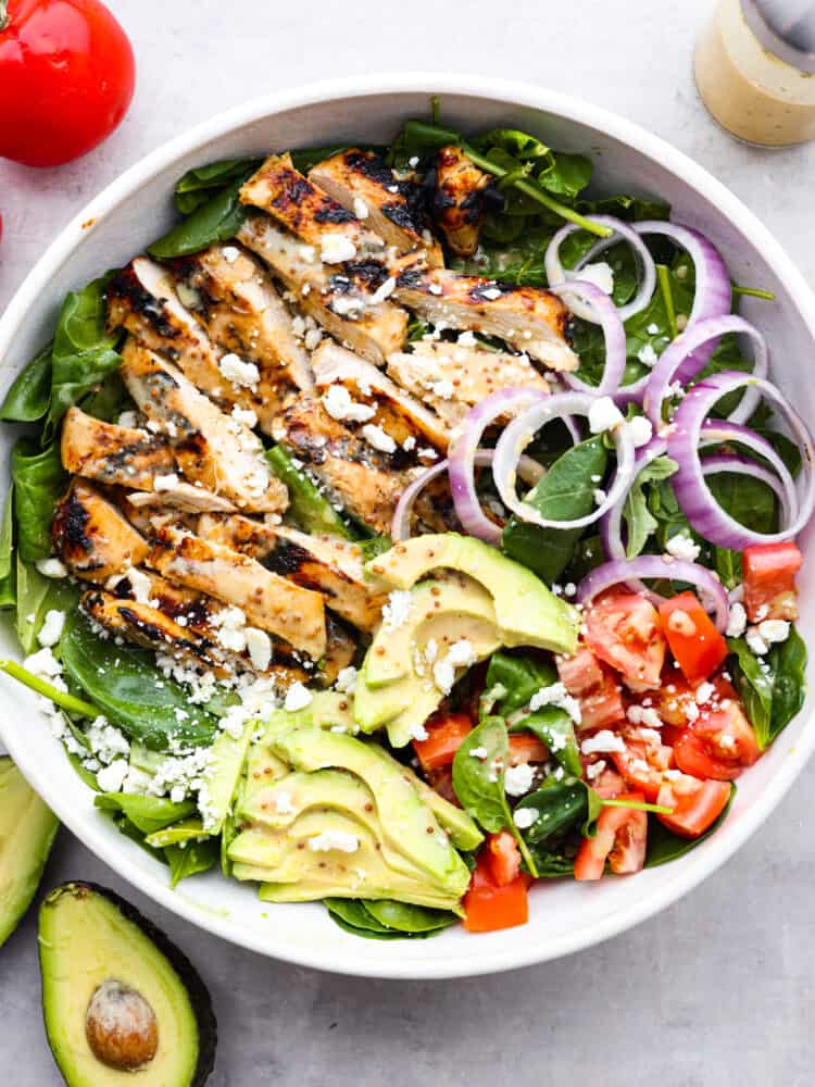 The top view of a honey mustard chicken salad with avocado, spinach, tomatoes, red onions and feta cheese. 
