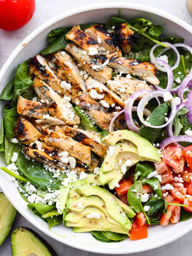 A salad bowl with spinach, avocado, honey mustard chicken, tomatoes, onions and feta cheese. 
