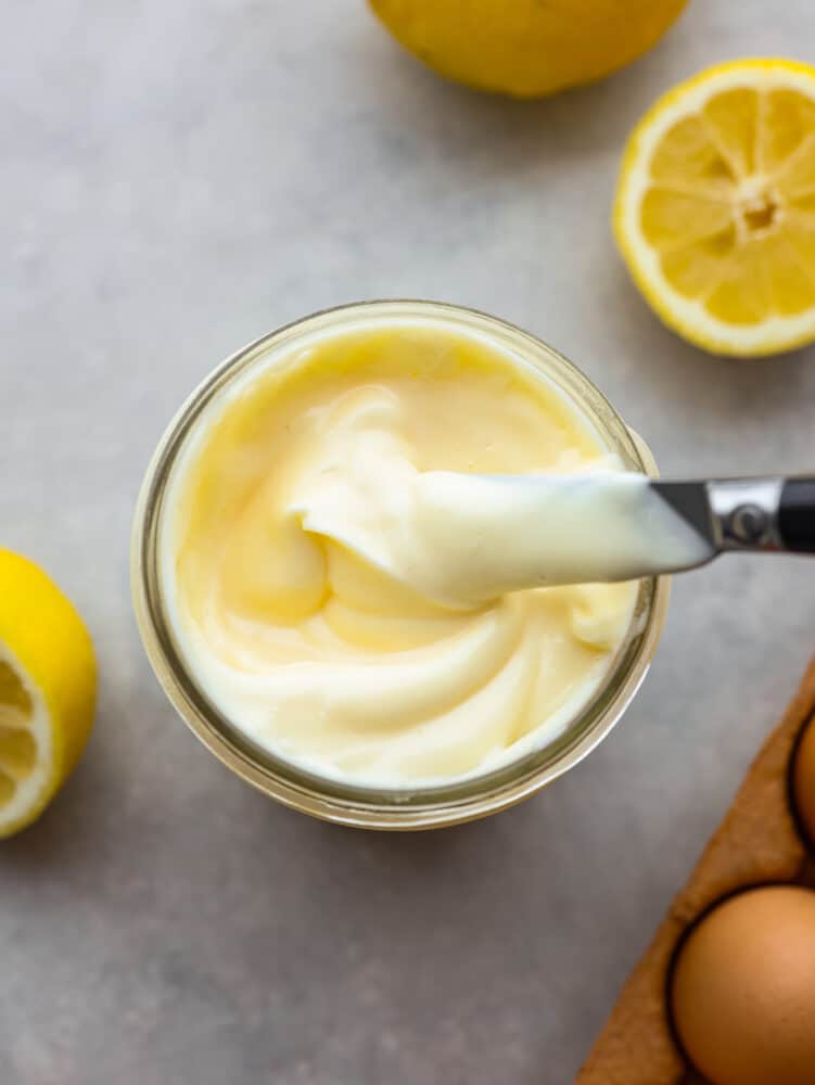 Bovenaanzicht foto van mayonaise in glazen pot met een mes bedekt met mayonaise en uit de pot tillen.