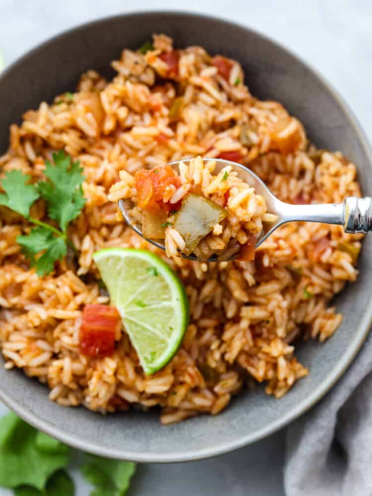 A close up of a bowl of Mexican rice with a silver spoon dishing some out. 