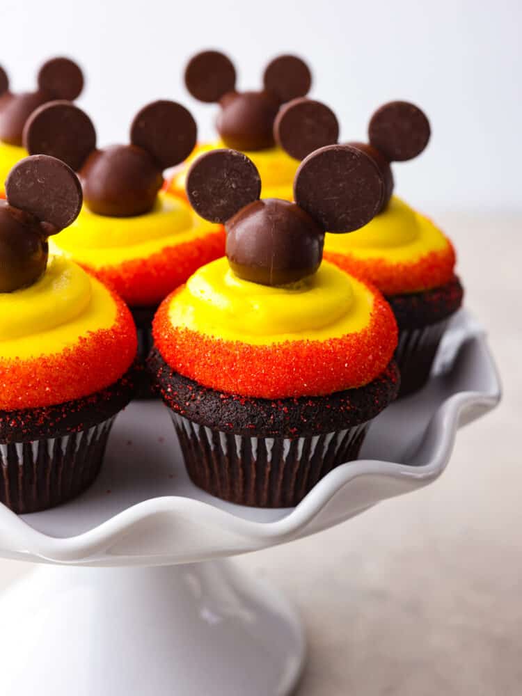 Mickey mouse cupcakes on a scalloped, gray platter. 