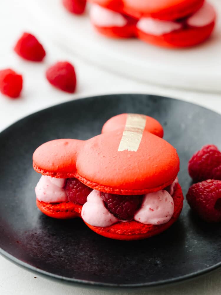 Closeup of a mickey macaron on a black plate, raspberry filling can be seen.
