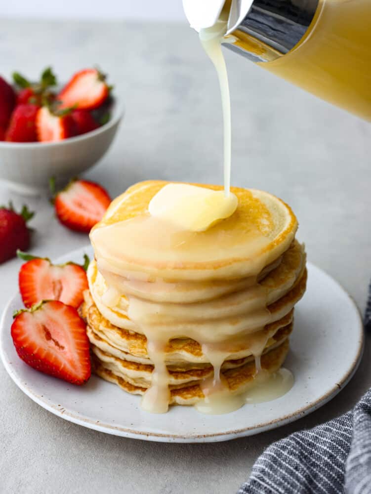 A stack of sour cream pancakes with coconut syrup being poured on them. 