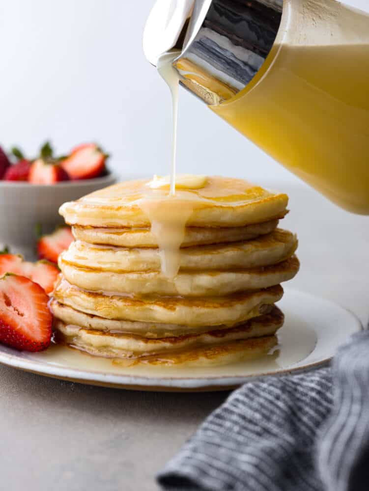 Pouring coconut syrup over a stack of pancakes.