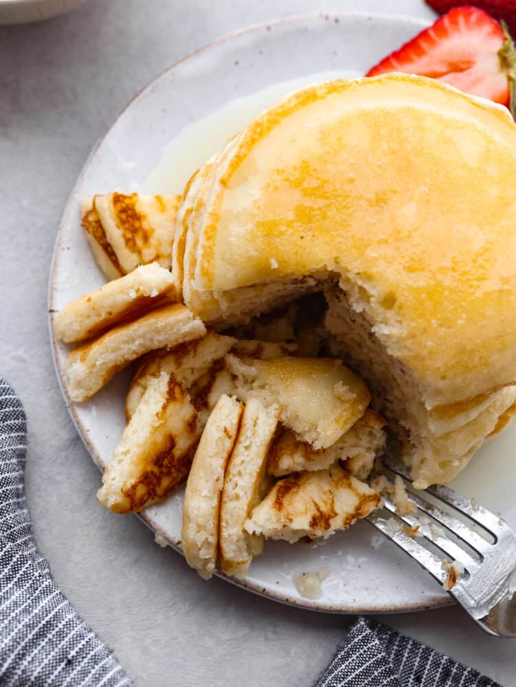 The top view of a stack of pancakes with a piece cut out with a fork. 
