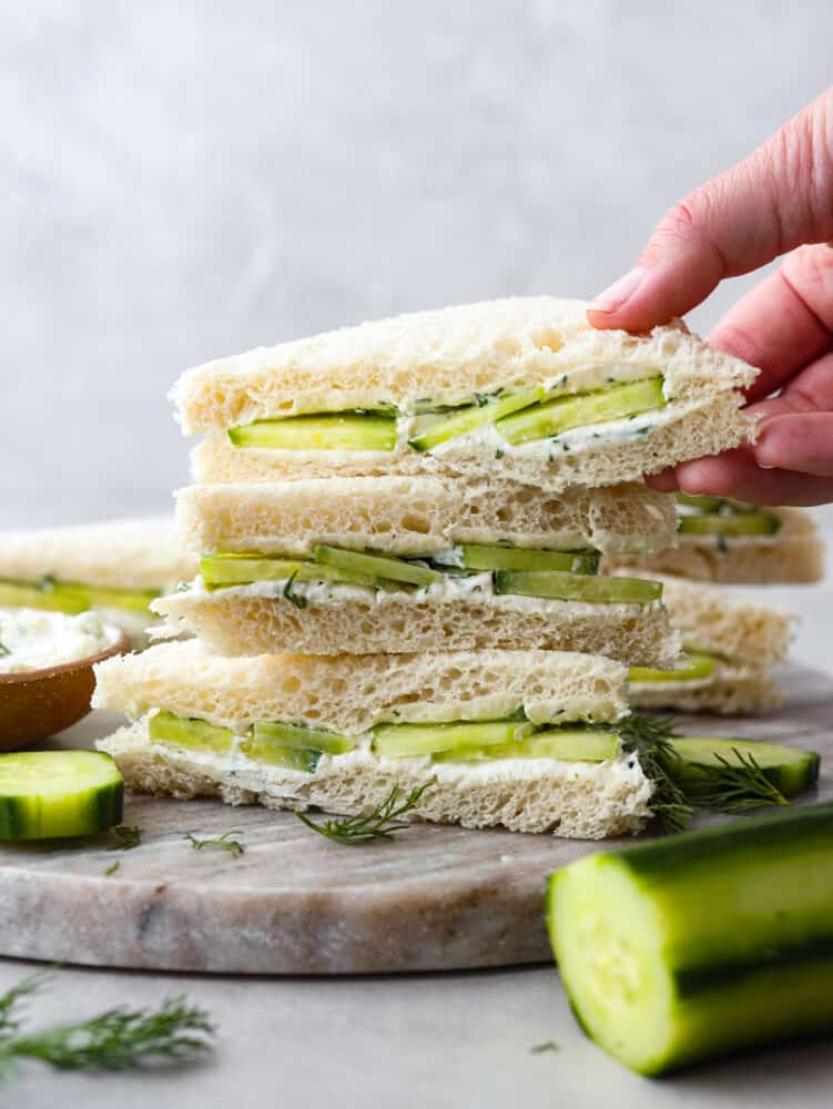 Front view of a stack of 3 cucumber sandwiches, the one on top stuff picked up.