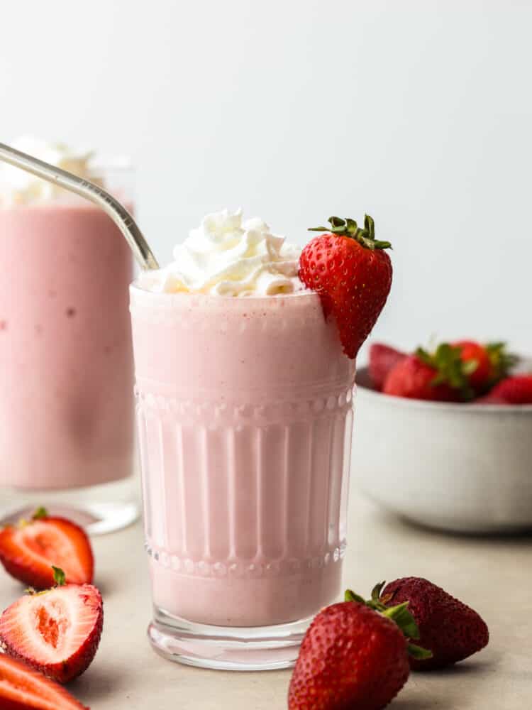 A strawberry milkshake in a glass with a silver straw and a fresh strawberries on the side. 