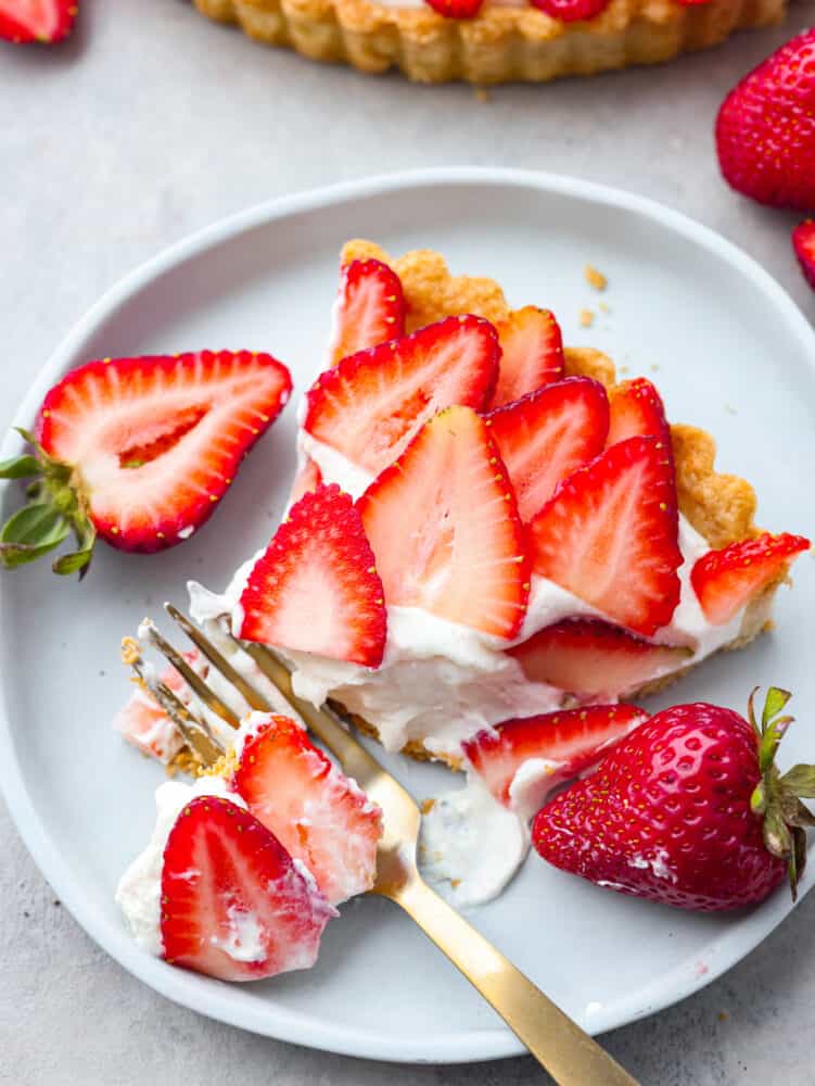 Taking a bite of strawberry tart with a gold fork.