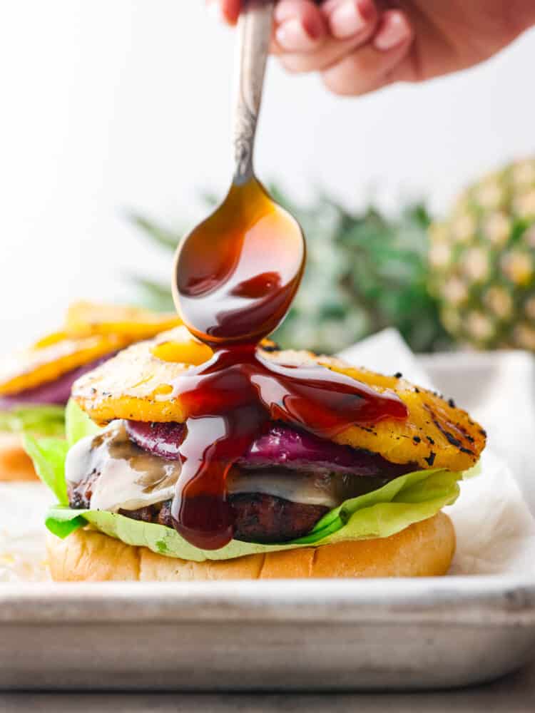 Teriyaki sauce being drizzled on the inside hamburger ingredients with a silver spoon. 