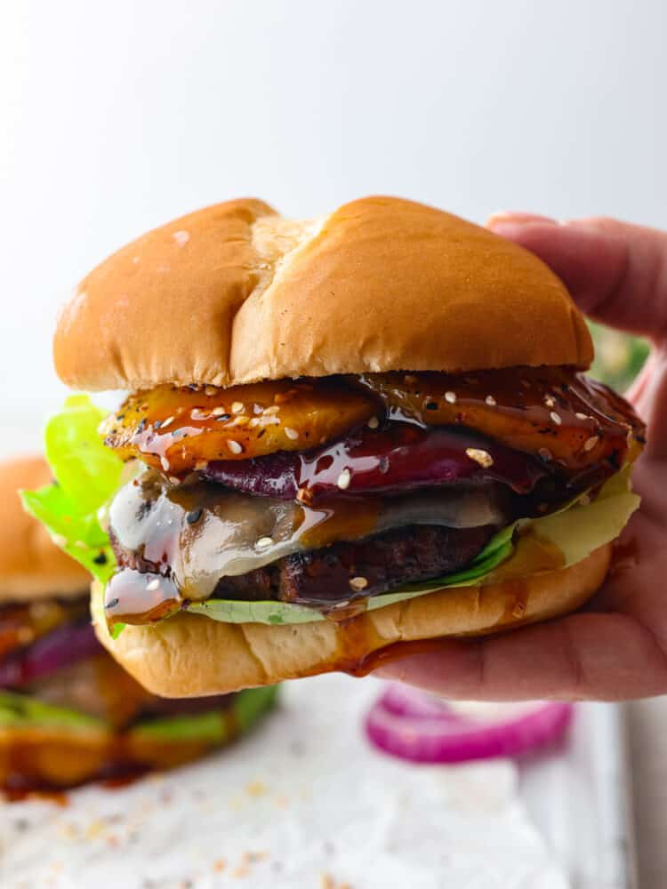 A hand holding a teriyaki burger that's ready to eat. 
