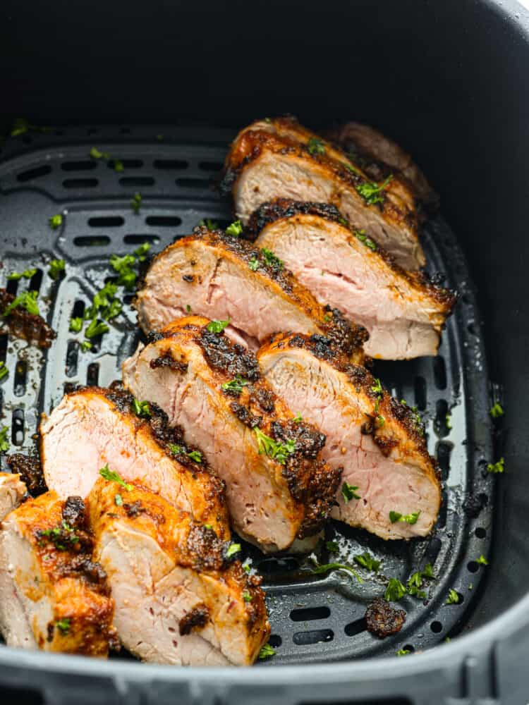 Top view of cooked sliced pork tenderloin in the air fryer.  Garnished with fresh parsley.