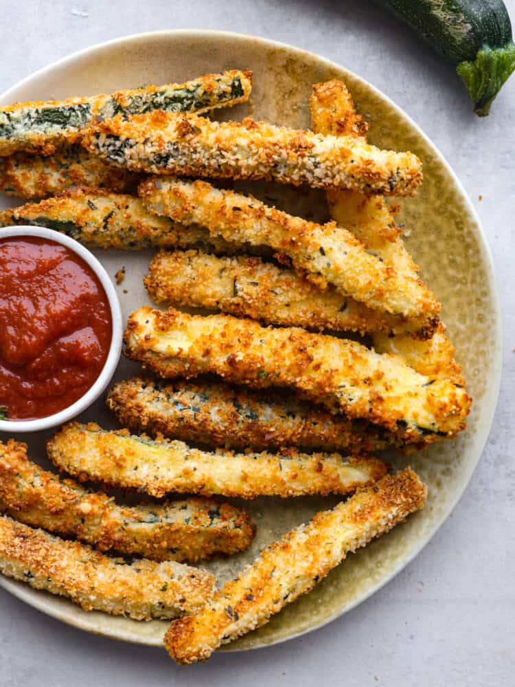 Air-fried zucchini fries served with marinara sauce on a gray plate.