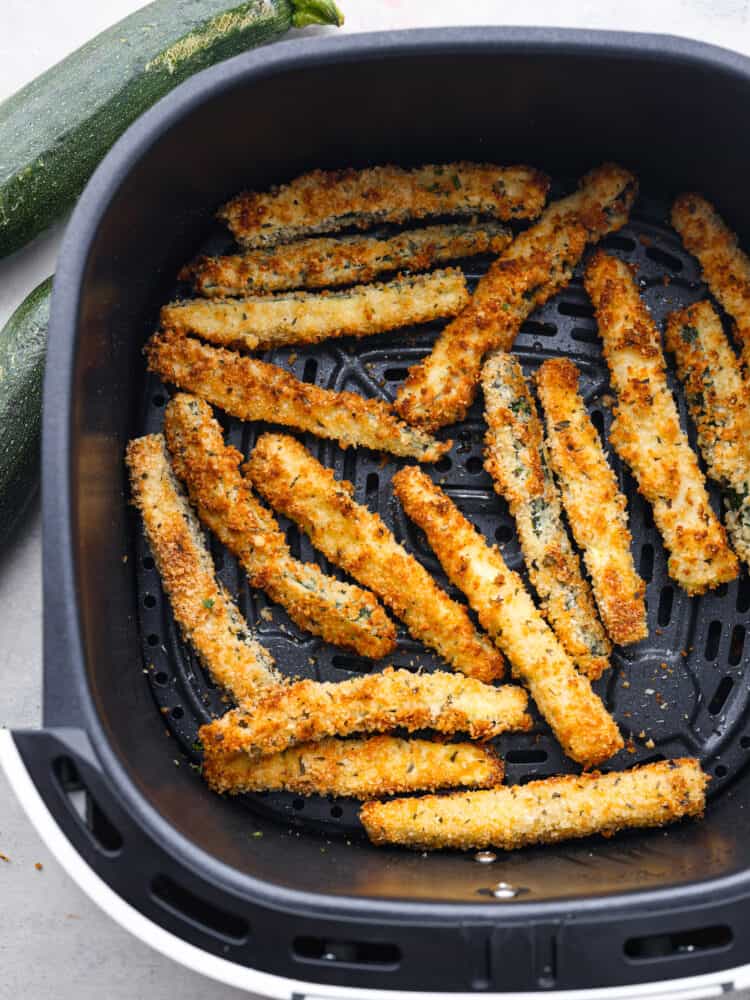 Cooked zucchini fries in the bottom of an air fryer basket.