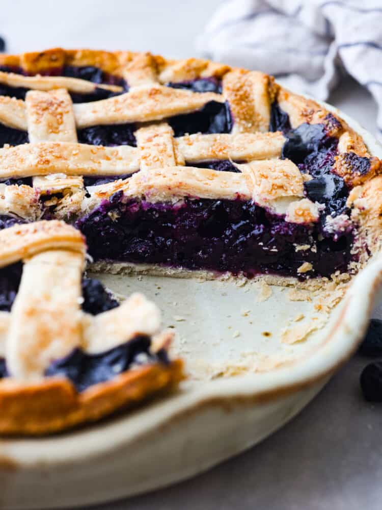 The side view of a blueberry lattice pie in a pie pan with a slice taken out. 