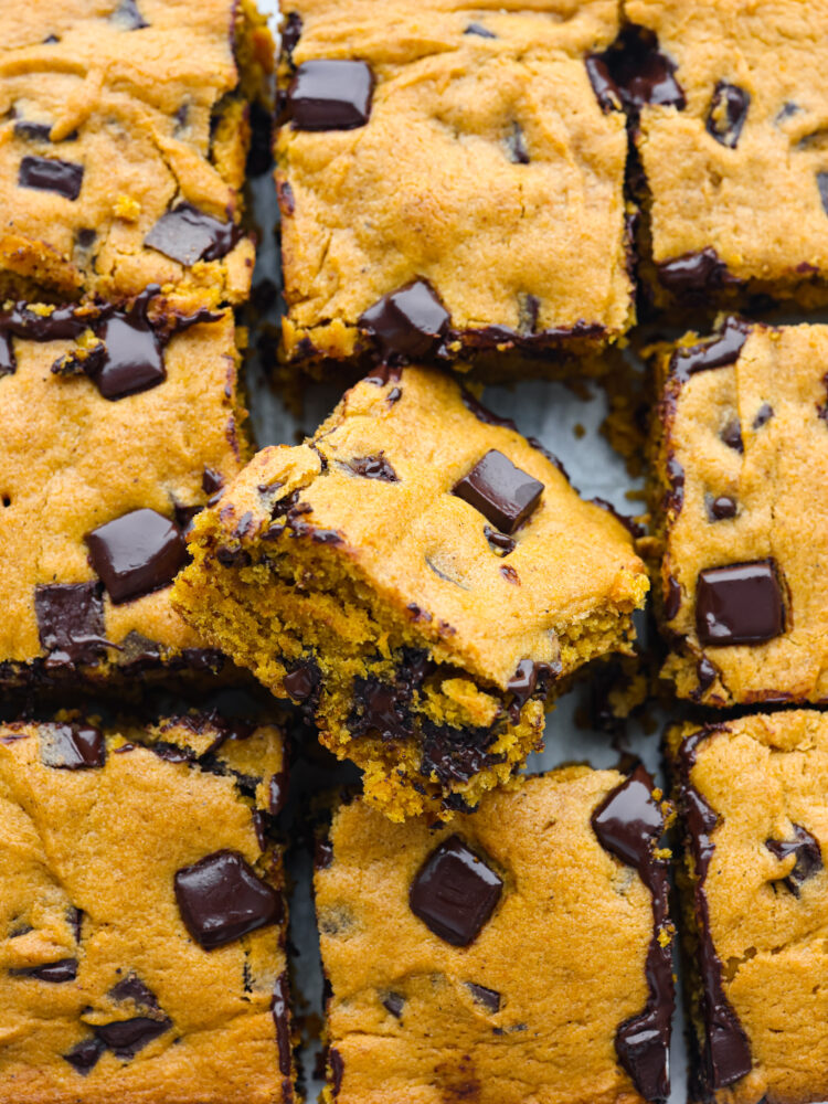 A close up of a pan of cooked pumpkin chocolate chip bars. One bar is slightly moved so that you can see the side of it. 