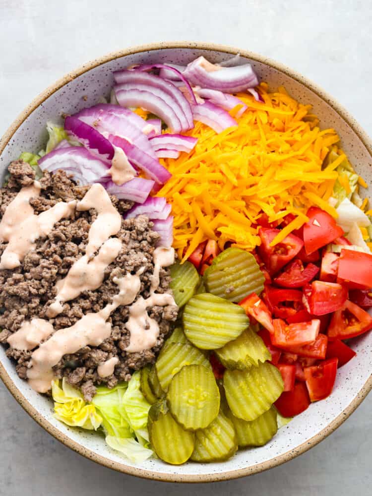 A top view of salad ingredients in a large bowl before they are tossed together.  The thousand island dressing is drizzled over the cooked meat.