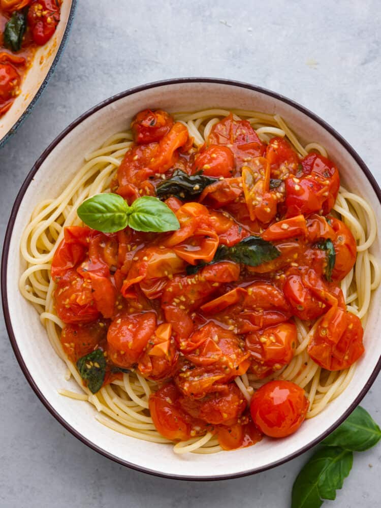 Overhead photo of pasta in a a white bowl with spaghetti noodles and cherry tomato sauce on top.  Fresh basil garnished on top and on the side.