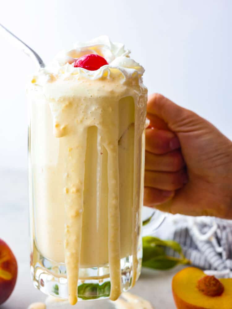 Holding a peach milkshake in a glass mug, with the milkshake spilling down the sides.