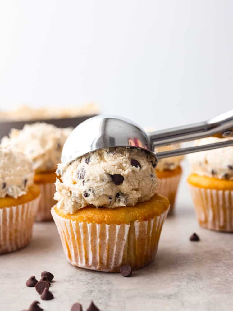 Adding a scoop of cookie dough frosting to a cupcake.