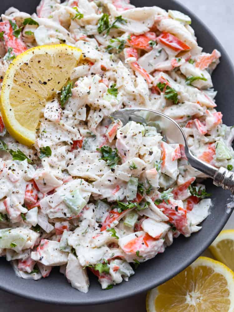 This delicious crab salad is hearty and cool, perfect for sandwiches or a side dish! Each bite is loaded with meaty crab, lemon, fresh herbs, and a hint of spice for flavor you won't be able to resist. Closeup of crab salad being scooped with a metal spoon.