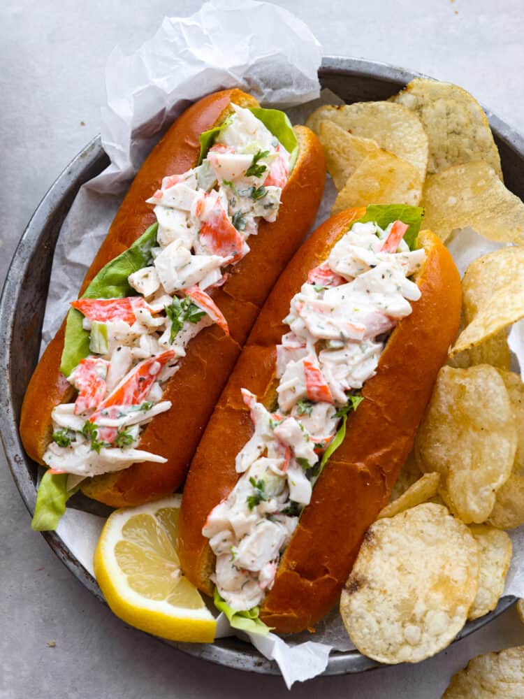 2 crab salad sandwiches on a gray plate served with potato chips.