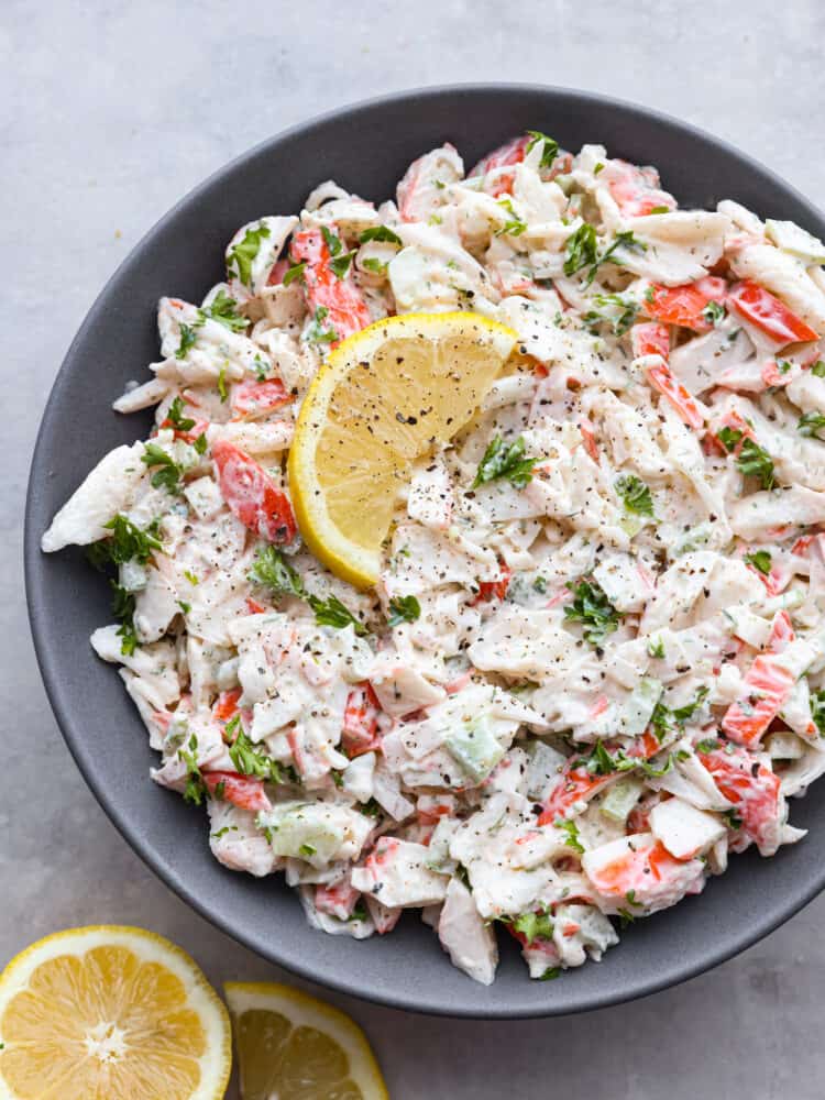 This delicious crab salad is hearty and cool, perfect for sandwiches or a side dish! Each bite is loaded with meaty crab, lemon, fresh herbs, and a hint of spice for flavor you won't be able to resist. Top-down view of crab salad in a gray bowl, garnished with a lemon.