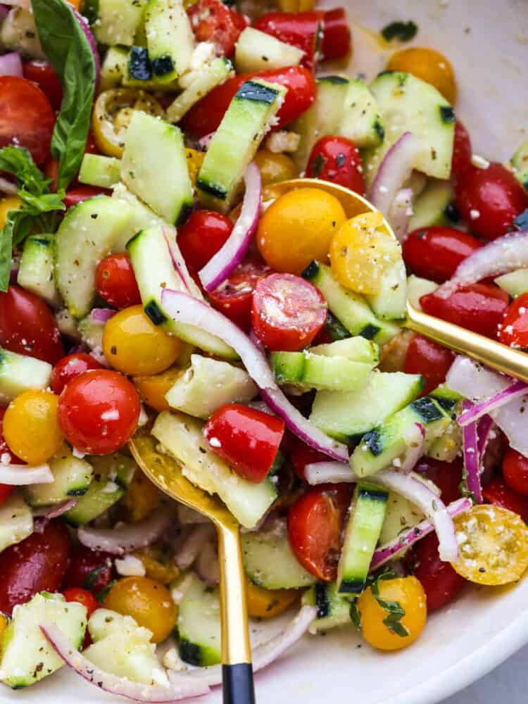 A close up of cucumber tomato salad in a bowl with a gold spoon. 