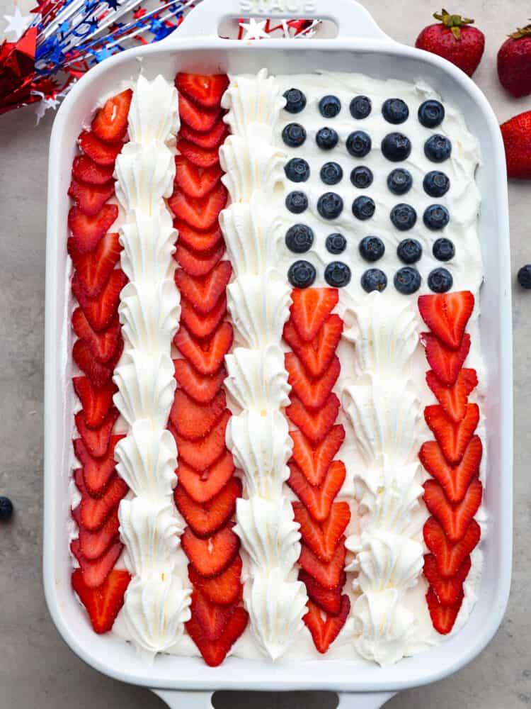 The top view of a rectangle cake with strawberrries, whipped cream and lueberries making it look like an American flag. 