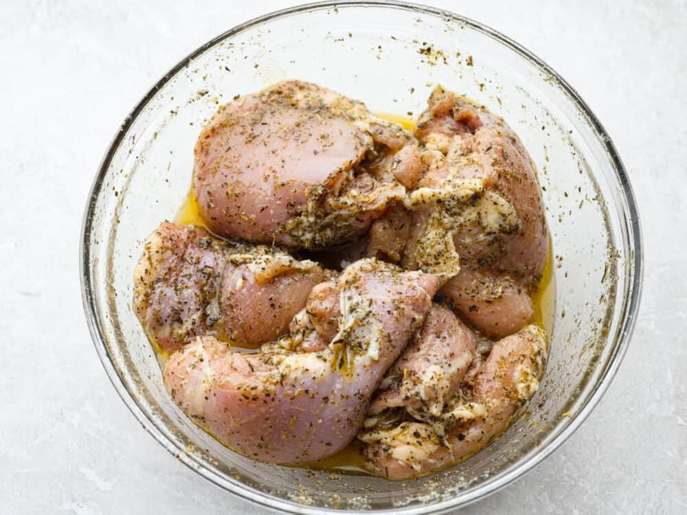A glass bowl of raw chicken covered iin a lemon marinade. 