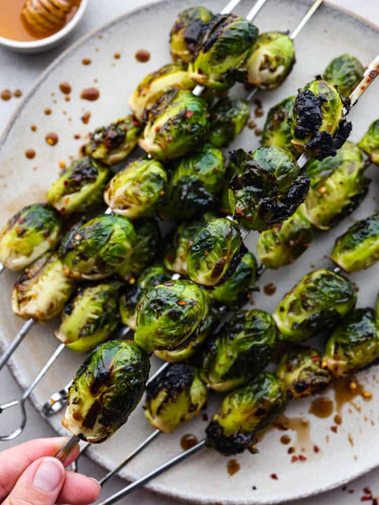 Crispy on the outside, tender on the inside, and topped with a balsamic honey glaze, these grilled brussels sprouts are the best side dish for summer and early fall! The amazing tangy flavor and tender, caramelized texture of these brussels sprouts will make even the pickiest of eaters a fan. A skewer of grilled brussels sprouts being picked up.