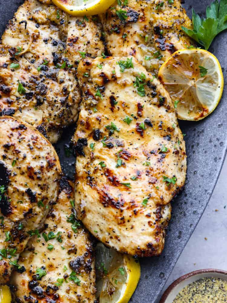 Grilled lemon pepper chicken on a platter with lemon slices. 