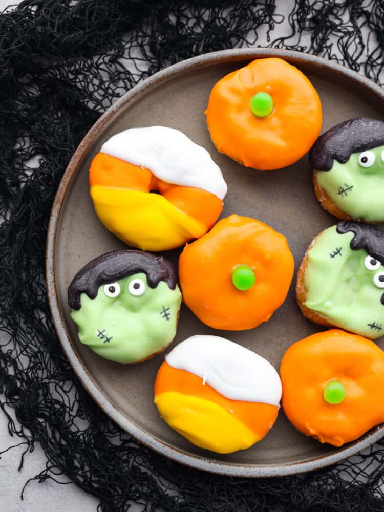 A platter of mini donuts that are decorated like candy corn, Frankensteing and a pumpkin. 