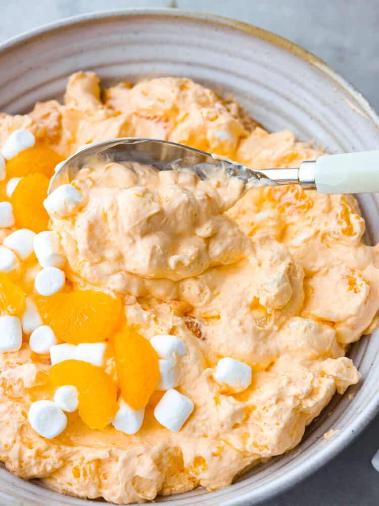 A bowl of orange creamsicle salad with a spoon scooping some out. 