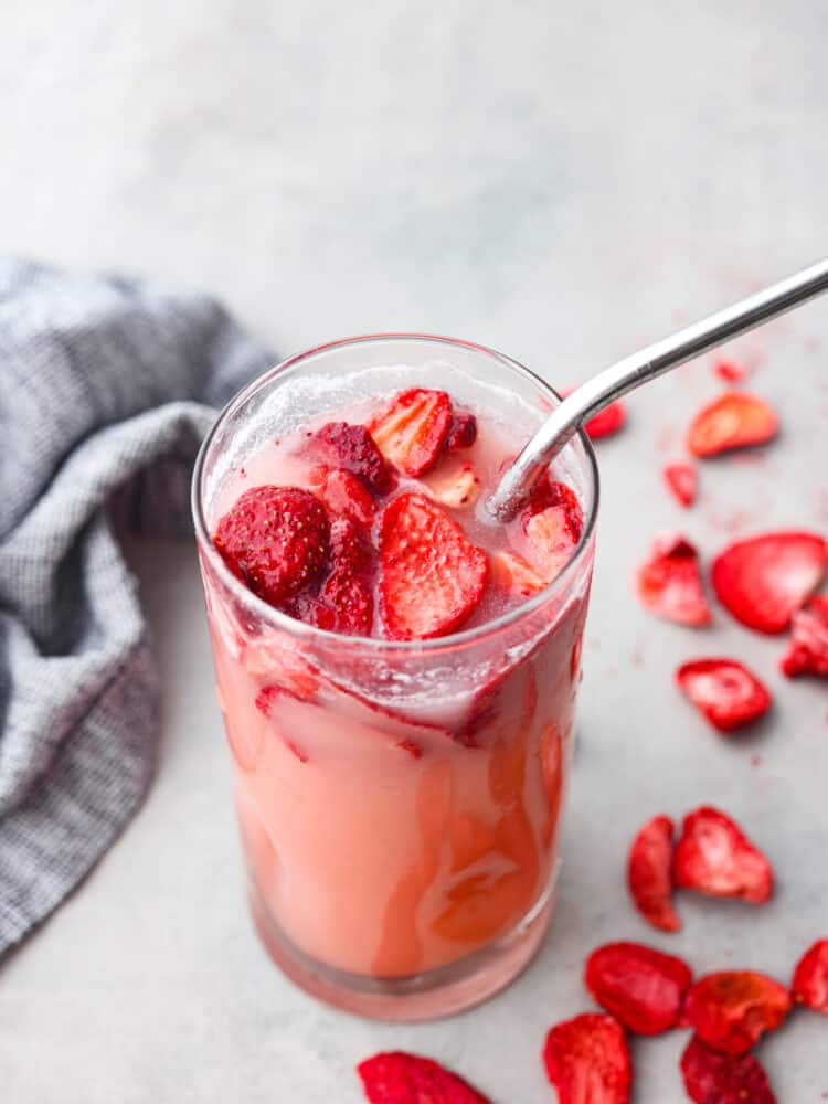 A pink drink in a glass cup with strawberries and a stainless steel straw.