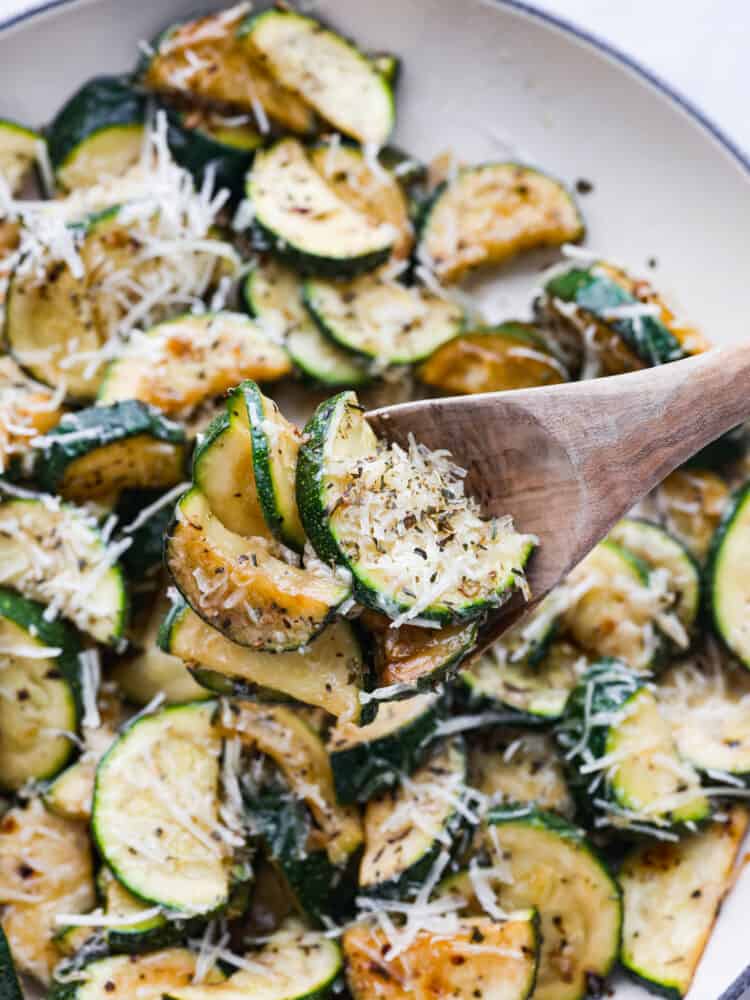 A close up photo of a wood serving spoon lifting the sautéed zucchini from the skillet.