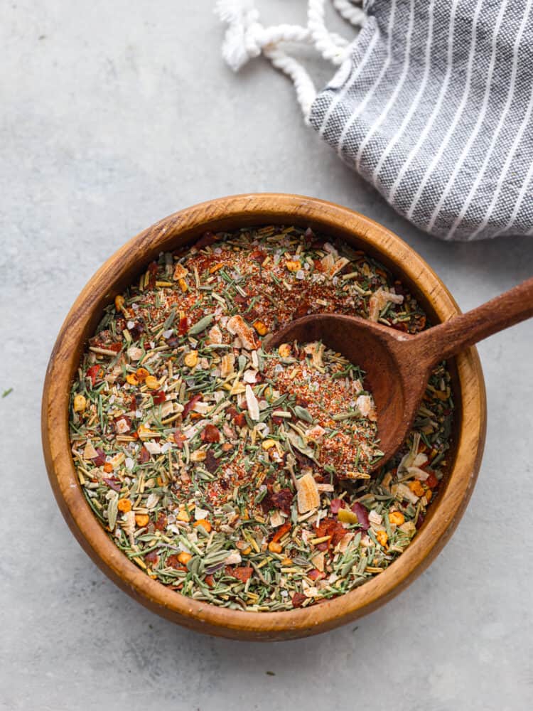 The top view of steak seasoning in a wooden bowl with a wooden spoon in it. 