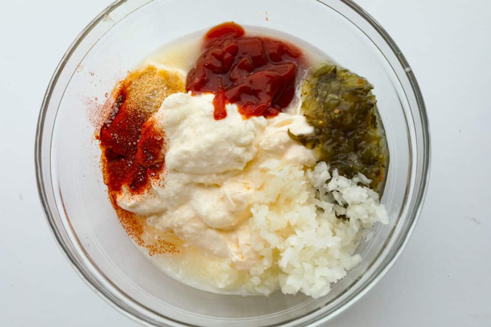 A clear, glass bowl filled with dressing ingredients that are ready to be mixed. 