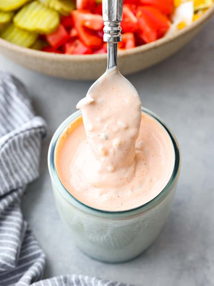 Thousand island dressing in a jar with a spoon being pulled out of it. 