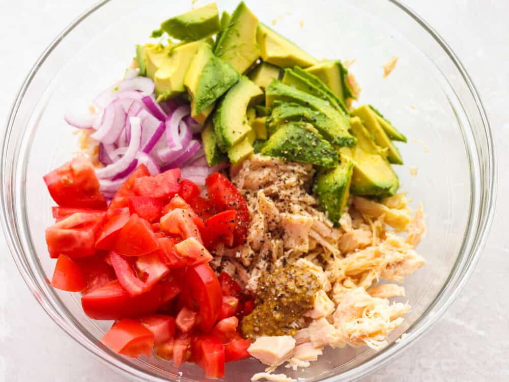 Ingredients for avocado tuna salad in a clear bowl, ready to be mixed.