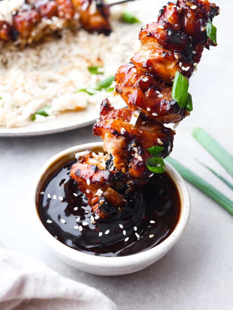 Dipping a grilled chicken skewer into yakitori sauce.