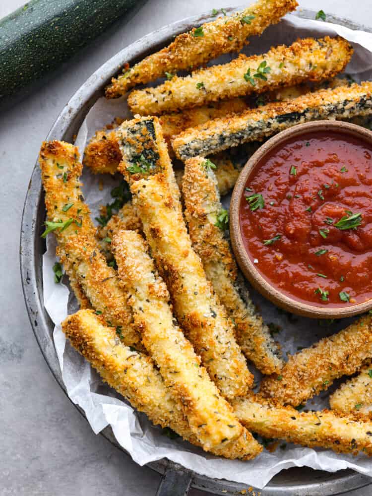 Top-down view of zucchini fries served with marinara sauce on a gray plate.