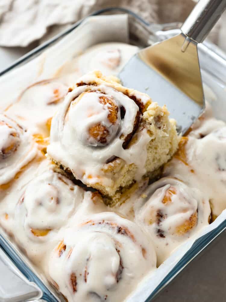 Baked cinnamon rolls in a 9x12 glass baking dish with one being served. 