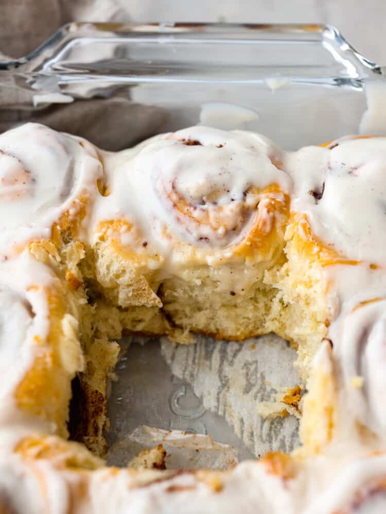 A pan with cinnamon rolls with one roll that is taken out. 