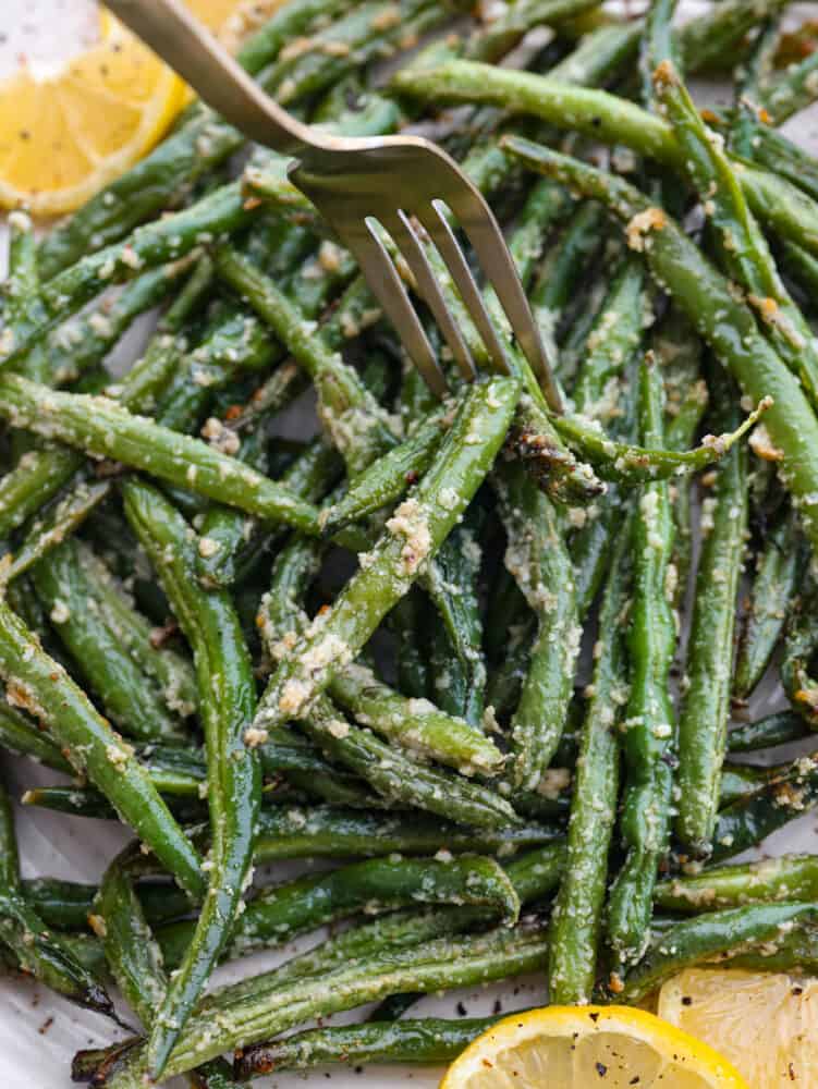 A close up shot of a fork in some cooked green beans. 