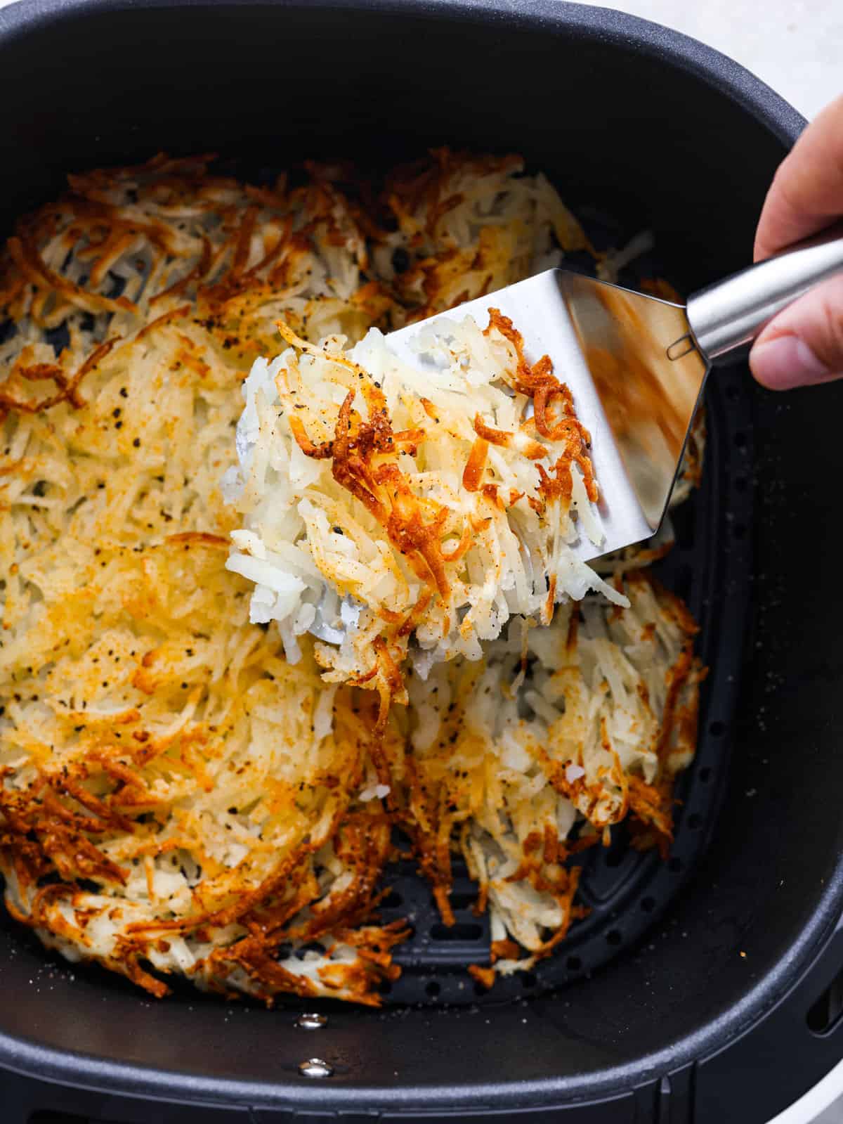 A picture of hash browns being served out of a pan. 
