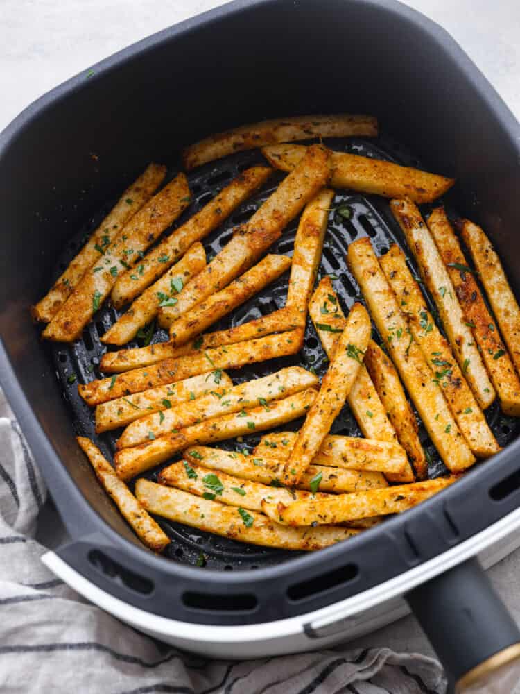 Vue de dessus du jicama de friteuse à air cuit dans un panier de friteuse à air.  Une serviette à main rayée est à côté du panier.