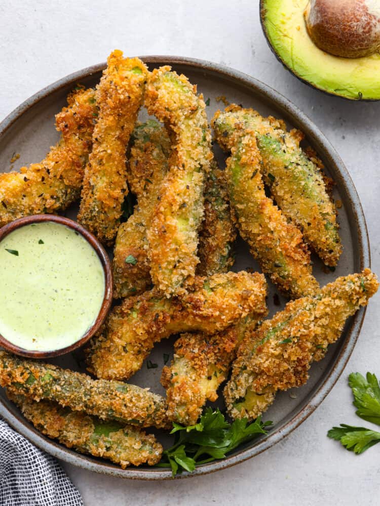 A round platter with baked avocado fries and a small bowl filled with avocado ranch. 