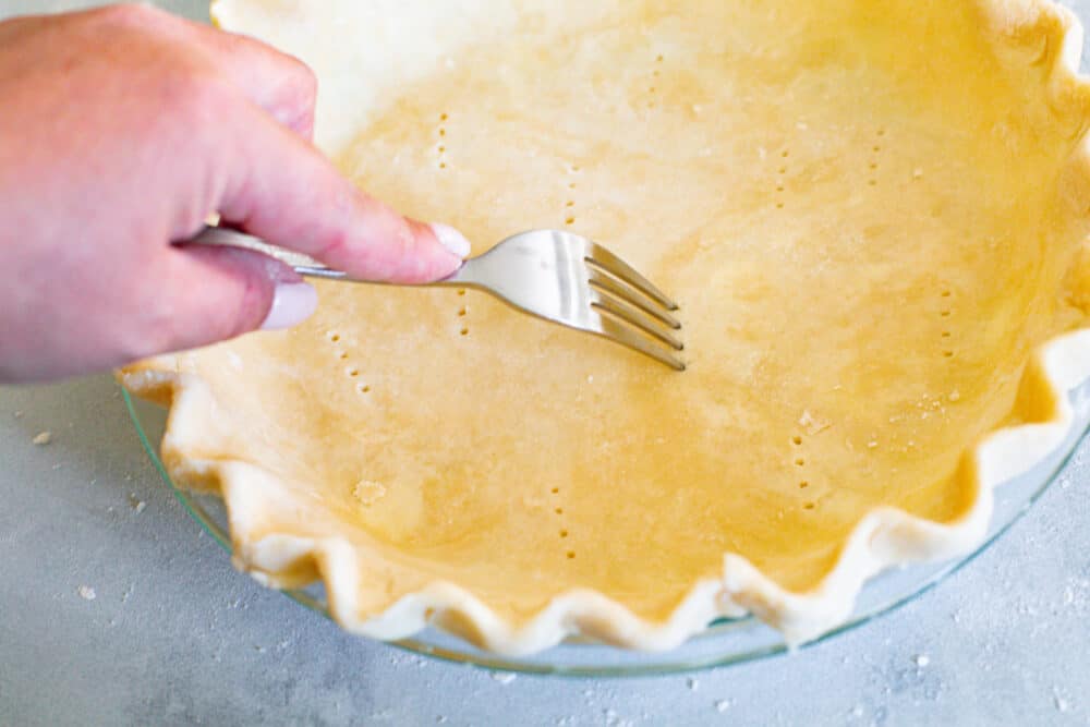 Pricking holes in the bottom of a pie crust using a fork.