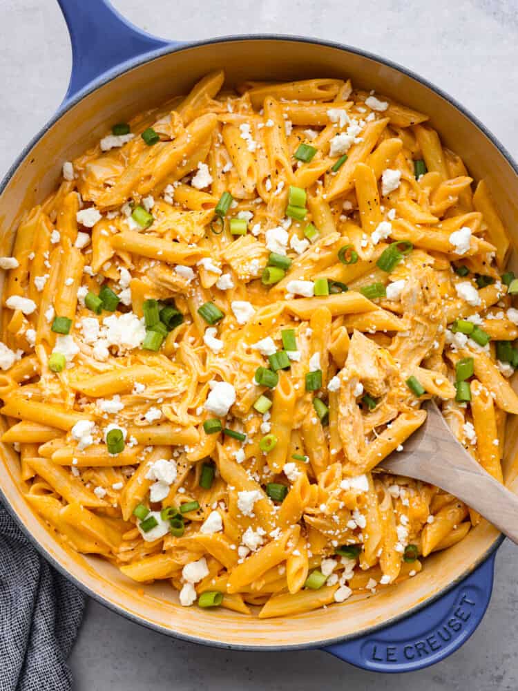 A skillet with cooked buffalo chicken pasta and a wooden spoon. 