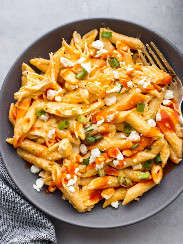 A gray bowl filled with buffalo chicken pasta garnished with blue cheese crumbles and green onions. 